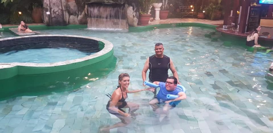 Young man with float, woman and man in thermal pool