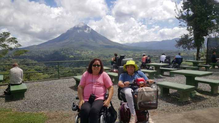 Two women in an electric wheelchair with the Arenal volcano in the background