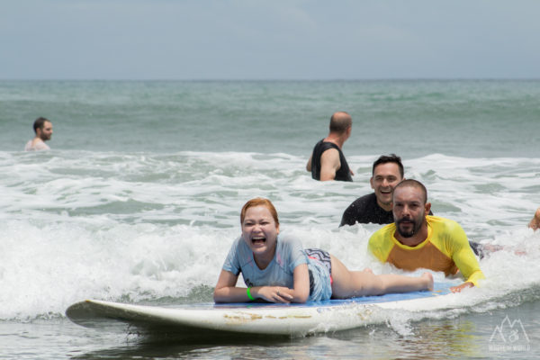 Side view of smiling woman lying on surfboard and instructors behind