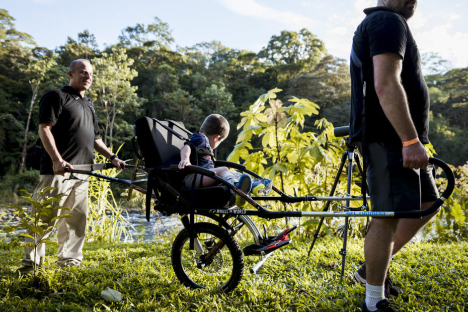 Kid in trekking chair assisted by two adults