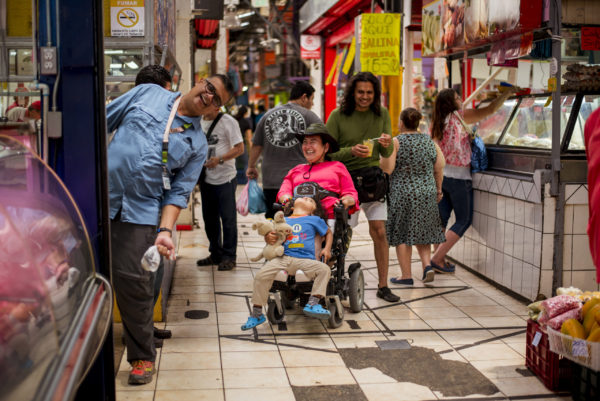 Woman in a wheelchair with child on her lap, walking with 2 men through the Central Market of San José