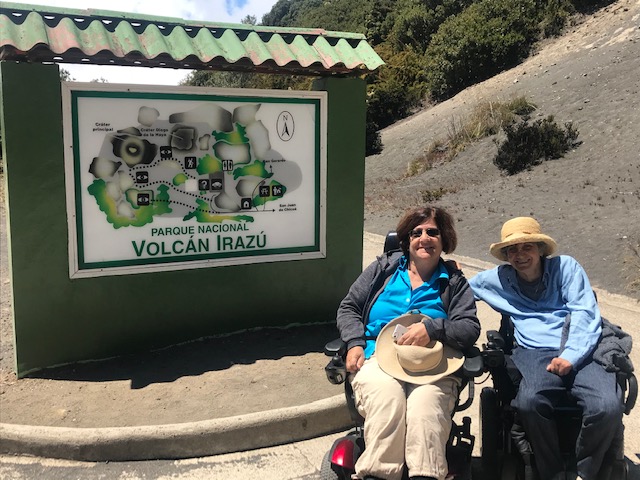 two women in an electric chair next to the irazú volcano sign